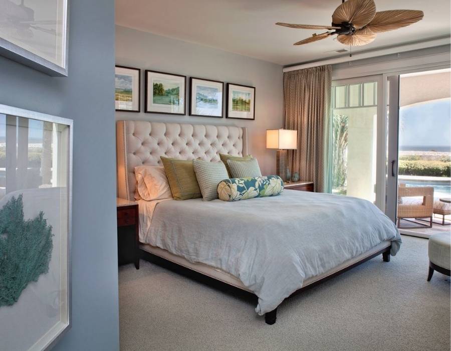 Elegant coastal bedroom with tufted headboard, tropical ceiling fan, ocean view, and serene decor in a Lowcountry home by Group 3 Designs.